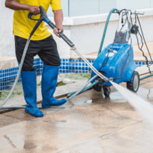 A man in a yellow shirt and blue shoes operates a pressure washer, cleaning a surface outdoors.